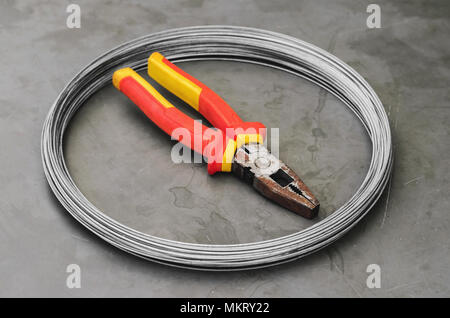 Coiled steel wire over a stone table with a used red plier on center. Carpentry and construction tools. Stock Photo