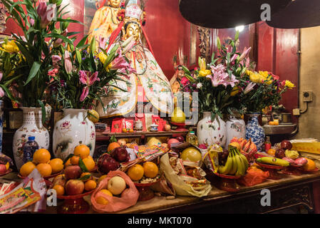 Fruits offerings, flowers in Chinese vases and golden statue of god in famous Man Mo temple, Sheung Wan, Hong Kong Stock Photo