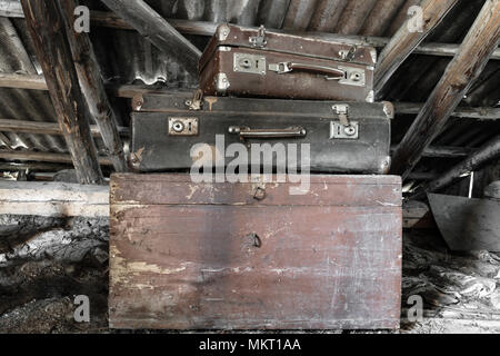 Two old, rusty, dusty and dirty brown and black suitcases lying on the brown chest in attic Stock Photo