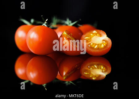 Reflected cherry tomatoes on the vine set against a black background Stock Photo