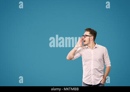 Young man in white shirt holding hand near mouth calling on yellow background. Stock Photo