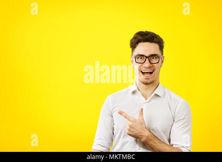 Young hipster man in glasses pointing happily away on orange yellow background Stock Photo