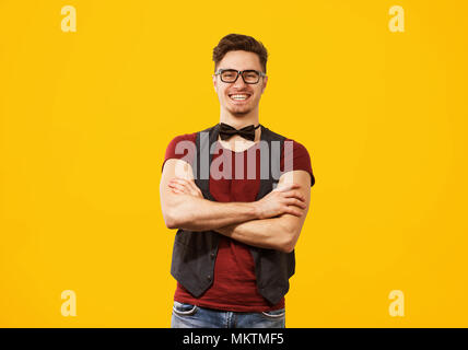 Handsome hipster man in eyeglasses and bow tie looking at camera with smile on yellow background. Stock Photo