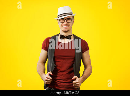 Closeup portrait of young succesful stylish hipster man in t-shirt, glasses and hat over a yellow background. Stock Photo