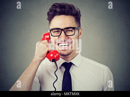 Handsome young man in eyeglasses talking on a phone and laughing at camera happily. Stock Photo