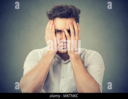 Young frustrated man covering face with hands looking unhappily at camera having trouble in life Stock Photo