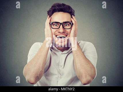 Young handsome man holding hands on face and looking stunned on gray background. Stock Photo