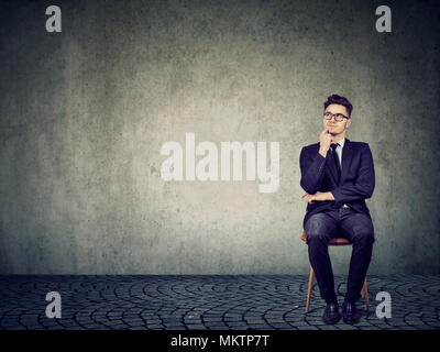 Formal man in eyeglasses sitting on chair and contemplating on strategy and making decision looking away. Stock Photo
