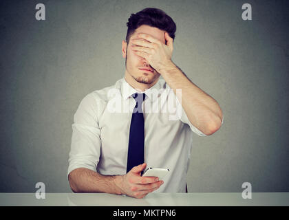 Young formal man using phone and covering face because of doing mistake while working Stock Photo