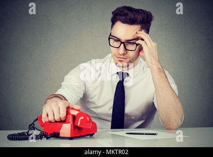 Young businessman at working table thinking carefully and making call solving problem. Stock Photo