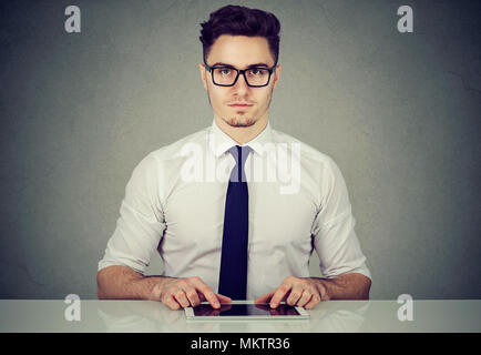 Young handsome man in glasses sitting at table working with tablet. Stock Photo