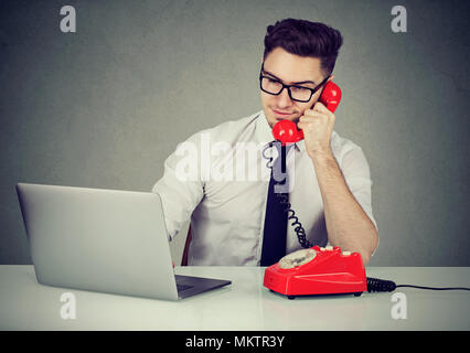 Handsome young man talking on telephone working as assistant with laptop at table. Stock Photo