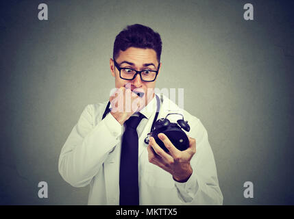 Stressed anxious doctor, health care professional holding alarm clock pressured by time isolated on gray background. Stock Photo