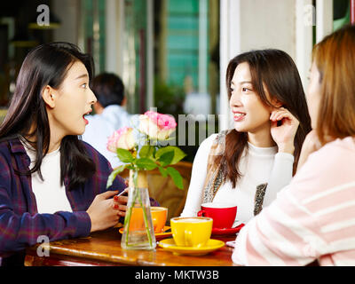 three happy beautiful young asian women sitting at table chatting talking in coffee shop or tea house. Stock Photo