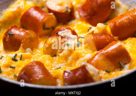 Breakfast of scrambled eggs and sausages in a pan on black background. Stock Photo