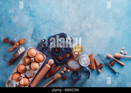 Making pastry flat lay with wooden scoops, whisks, cookie cutters, muffin tin, sugar, flour, eggs and cinnamon on a modern concrete background with copy space. Baking tools and ingredients from above. Stock Photo