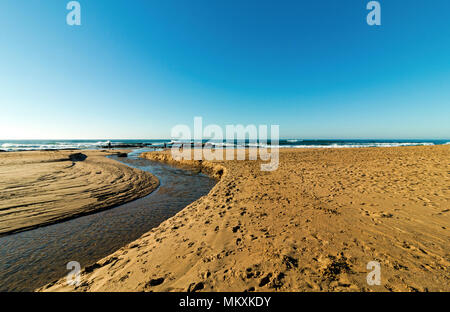 Landscape view of river estuary rippled water flowing through patterned and textured golden beach sand against blue coastal skyline in South Africa Stock Photo