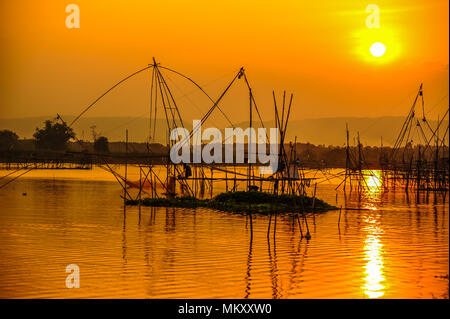 Fisherman working on bamboo scaffolding with traditional bamboo fishing tools in swamp in evening time. Stock Photo