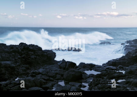 Waves at first light pound the lava shoreline around the Queens Bath on Hawaii’s Island of Kauai. Stock Photo