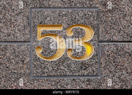 Number 53 inclosed in a square frame painted in gold color on a stone wall. Stock Photo