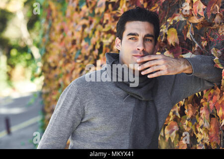 Handsome man wearing winter clothes in autumn leaves background. Young male with swater and scarf. Stock Photo