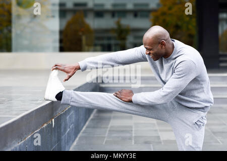 Black man doing stretching before running in urban background. Young male exercising Stock Photo