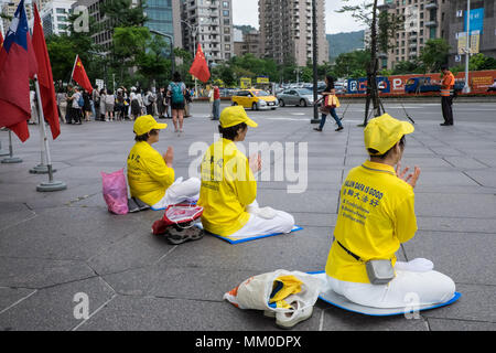 Mainland Chinese tour groups at the base of Taipei 101 Tower,attract two demonstrations,Taipei,Taiwan,Asia.The mainland Chinese tour buses park infront of Taipei 101 Tower,the second tallest building in the world,for the mainland Chinese to access this tourist attraction. On disembarking and getting on the buses nationalist Chinese supporters welcome them flying the Chinese flag.The pro-China supporters are there as a counter-demonstration to another group of demonstrators,the Falun Dafa/Falun Gong that have placards protesting about the persecution of members of the banned organization within Stock Photo