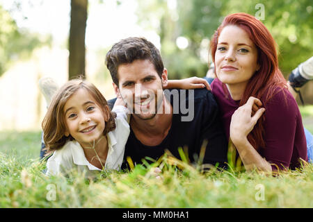 Happy young family in a urban park. Father, mother and little daughter laying on grass. Stock Photo