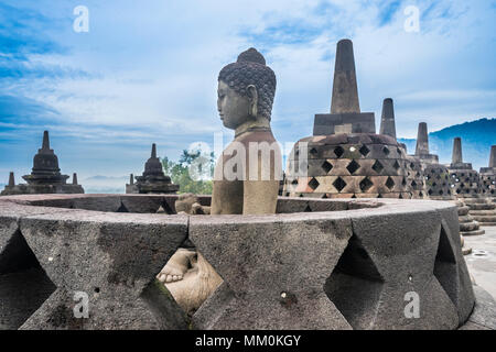 an exposed Buddha statue in an opened perforated stupa on the circular top terrace of 9th century Borobudur Buddhist temple gazes serenly over the Ked Stock Photo