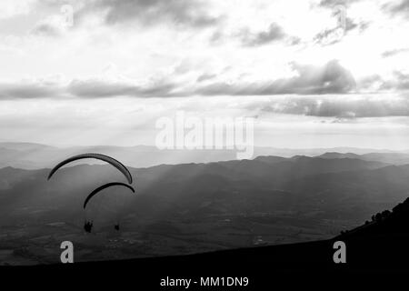 Some paragliders flying over a mountain scenery, with some faint sunrays in the background Stock Photo