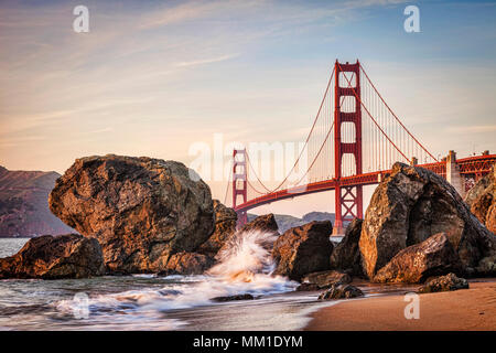 Golden Gate Bridge, San Francisco, approaching sunset., with a wave splashing up against rocks.