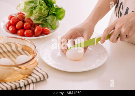 Close up of females hands cutting boiled egg for his breakfast and mixed vegetables on white wooden background Stock Photo