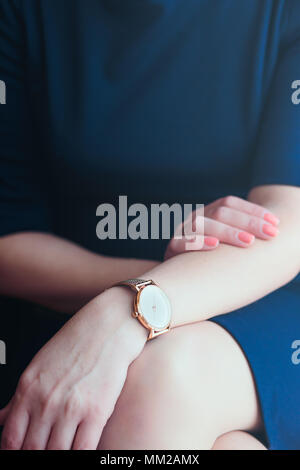 Elegant woman wearing gold wristwatch with bracelet and blue dress holding hands on her legs Stock Photo