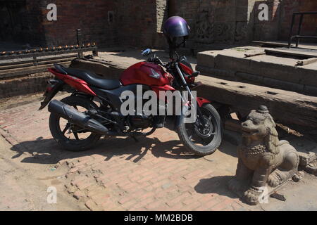 Bhaktapur, Nepal - March 23, 2018:  Modern motorcycle and ancient lion statue Stock Photo