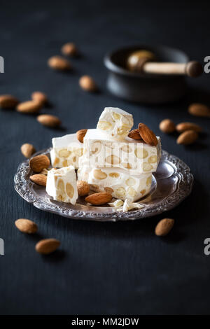 Delicious Italian festive torrone or nougat with almonds on a vintage plate against black wooden background Stock Photo