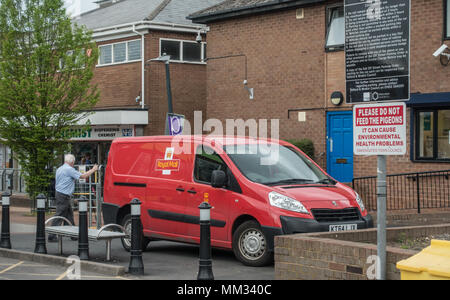 A postman loading up his van with parcels from the local post office, whilst parked on the pavement in a pedestrain area Stock Photo