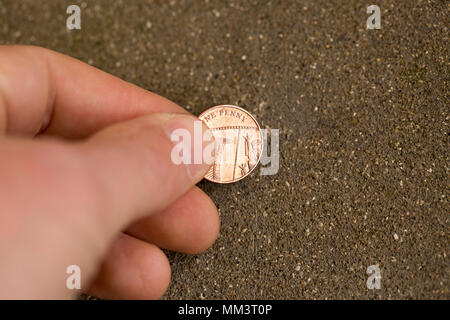 Posed picture of picking up a one pence piece from the ground. UK Stock Photo