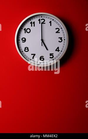 Five o clock. Clock hanging on the red wall. Stock Photo