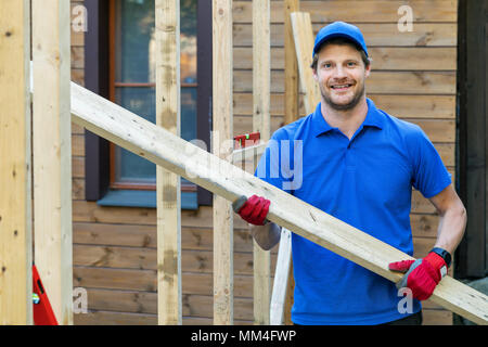 worker with wooden plank in hands at construction site Stock Photo