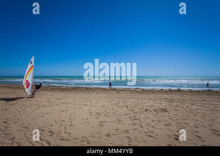 People walking on a beach on a sunny day and man preparing windsurfing, Bibione beach, Venice, Italy Stock Photo