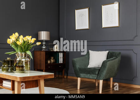 Green armchair against grey wall with posters in modern living room interior with flowers Stock Photo