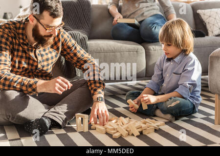 Father arranging wooden bricks with his son while sitting on carpet Stock Photo