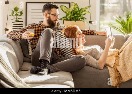 Man drinking juice while spending time with his wife reading book at home Stock Photo