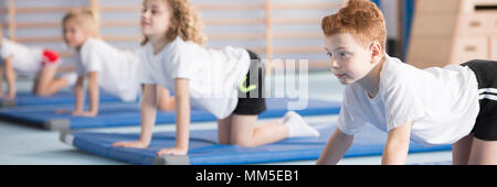 Young boy exercising on a blue mat during corrective gymnastics classes at school Stock Photo