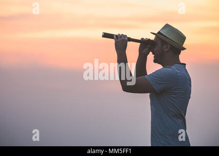 Young tourist looking through spyglass against orange sky at sunset. Space for copy. Stock Photo