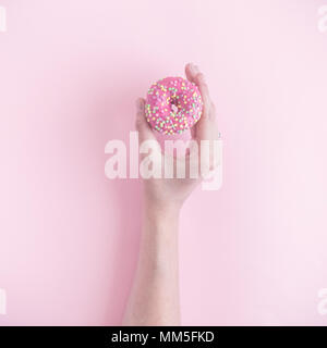 Close up of female hand holding small donut on pastel pink background minimal creative concept. Stock Photo