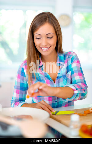 Beautiful young woman cooking healthy meal in the domestic kitchen and adding the spices by the fingers. Stock Photo