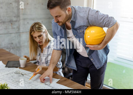 Young worried architect colleagues talking and analyzing blueprints while working on a new project at the office. Stock Photo
