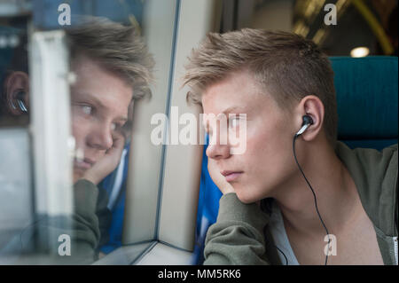 Boy listening music on headphones and looking out of window in train, London, England Stock Photo
