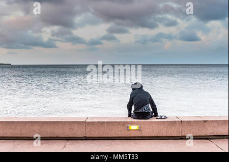 A solitary young man site alone on the beach walk looking out to sea in Cairns, Australia. Stock Photo